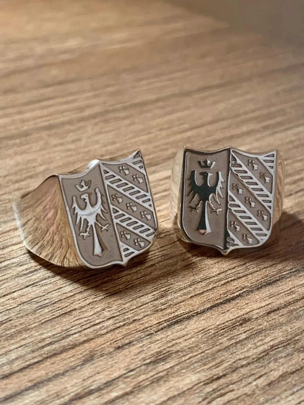 Dos anillos sello Égida con escudo en relieve, sobre una mesa de madera